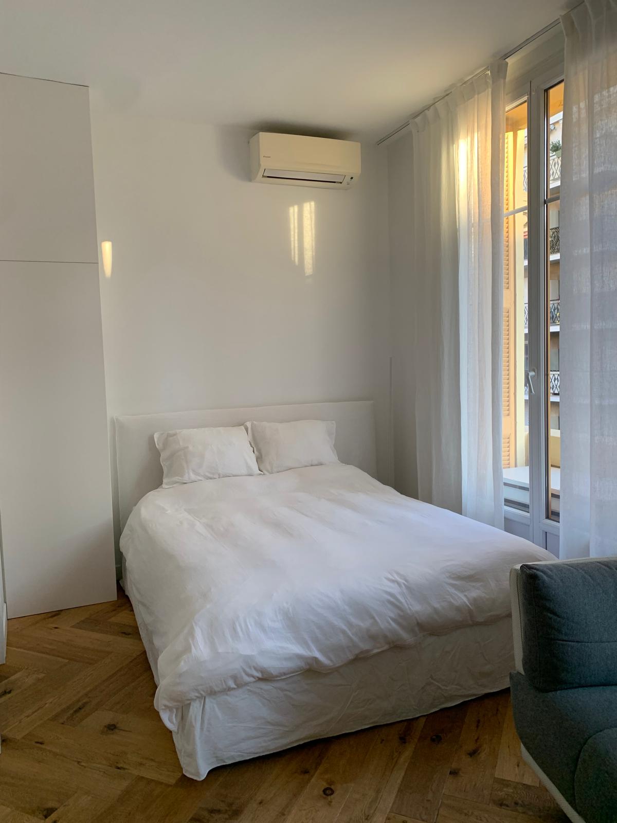 Lit double avec linge blanc près des hautes fenêtres à la française et de légers rideaux