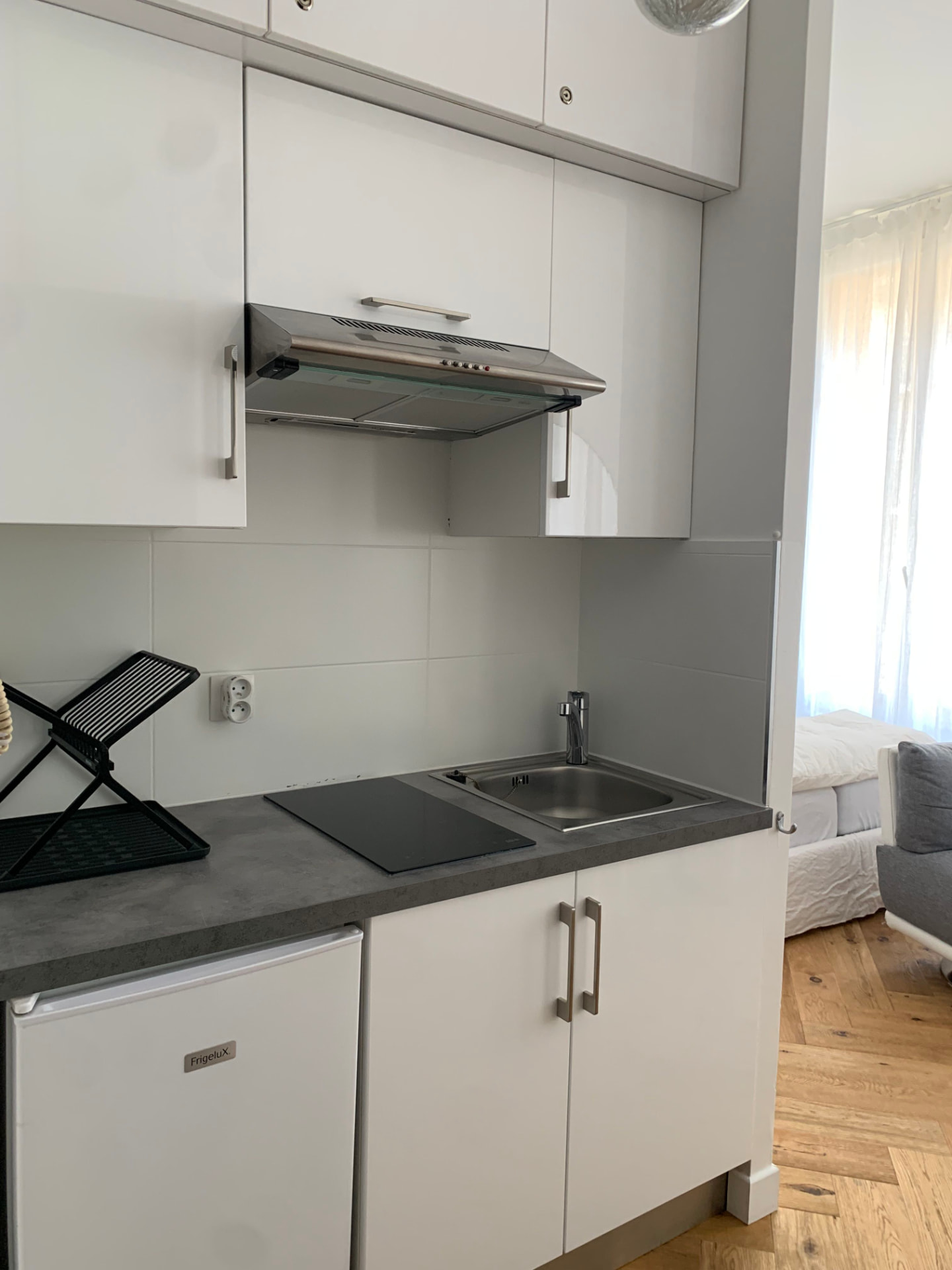 Kitchenette blanche et compacte avec plaque à induction, évier en inox et hotte aspirante