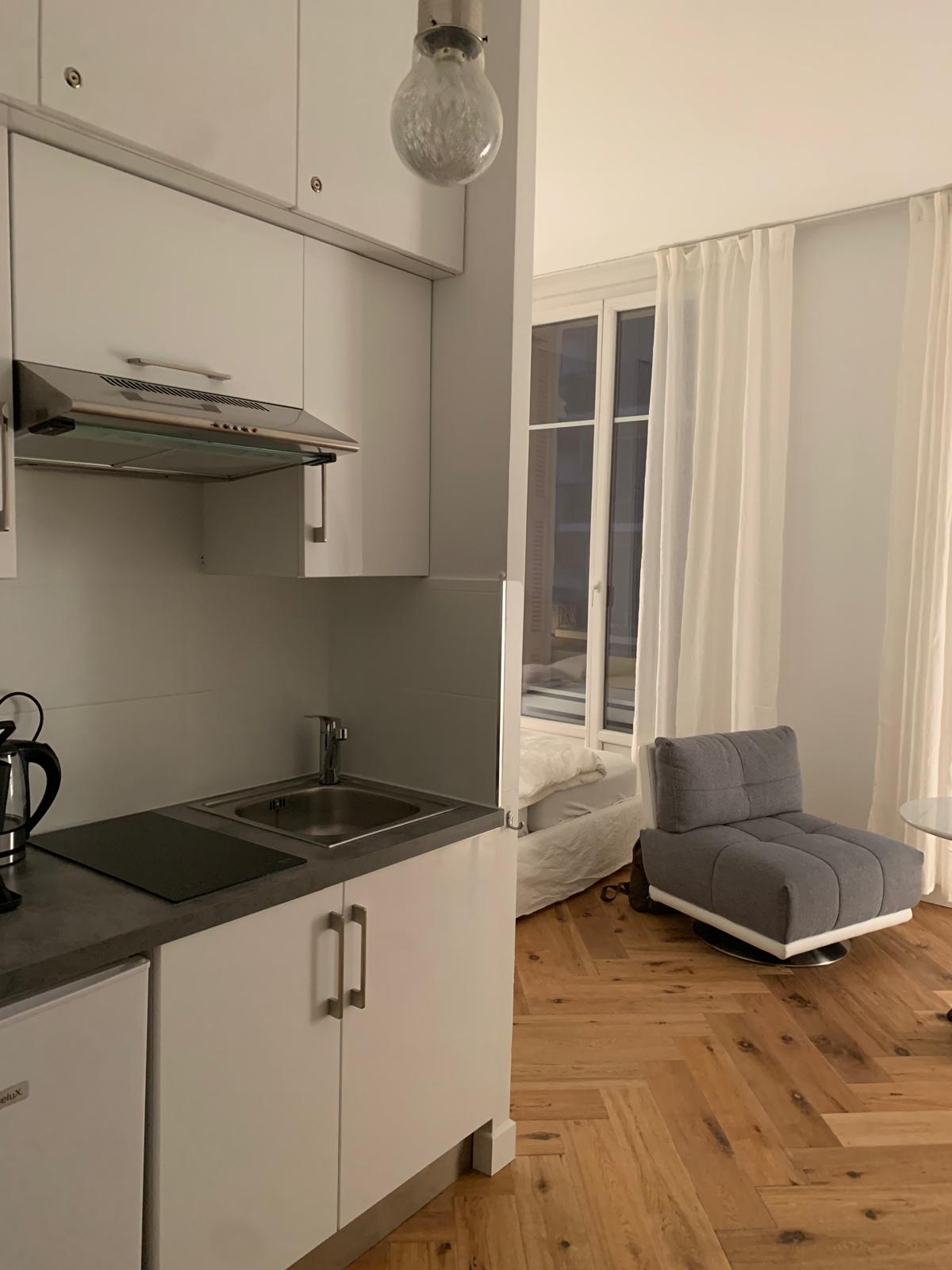 Kitchenette mit Kochfeld, Spüle und Kühlschrank neben der Sitzecke des Studios und der Fenstertür