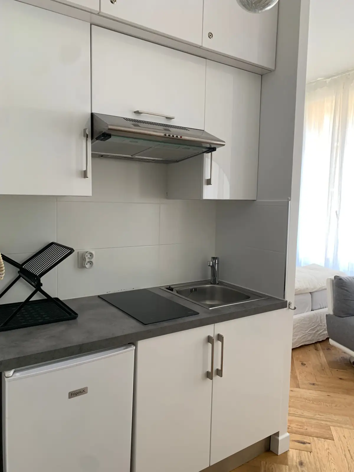 Compact white kitchenette with induction hob, stainless sink and extractor hood